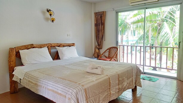 Un dormitorio con cabecera de madera, cama con ropa de cama blanca, un tapete verde en el suelo y vistas a palmeras a través de una puerta corrediza.