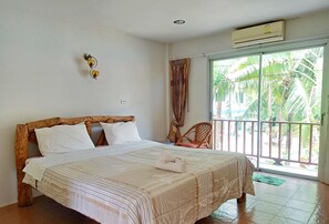 A bedroom with a wooden headboard, a bed with white linens, a green mat on the floor, and a view of palm trees through a sliding door. - Wangnamkam Riverside Resort (That Phanom)