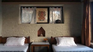 A room with two beds, a small table, a decorative wall piece, and a window with curtains.