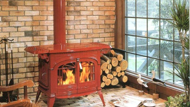 A red wood-burning stove with a brick wall and a window in the background.