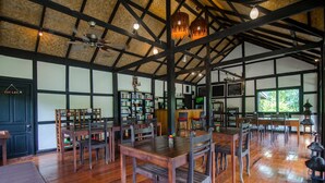 A spacious room with wooden floors, a high ceiling with exposed beams, and a large bookshelf filled with books.