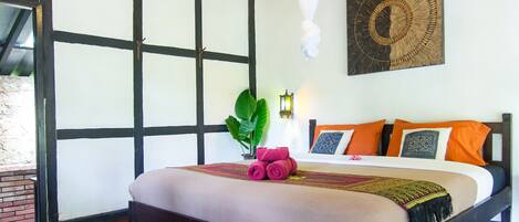 A bedroom with a wooden ceiling, a bed with orange and black pillows, and a large window.