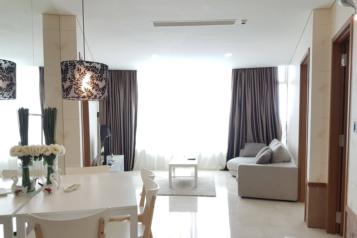 A modern living room with a white sofa, a dining table with chairs, and a large window with curtains.