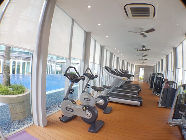 A gym with treadmills, elliptical machines, and weight machines, large windows, and a view of a water body.