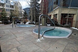 Zona de piscina con dos jacuzzis, suelo de piedra y edificios circundantes.