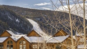 A row of log cabins with snow-covered roofs, set against a backdrop of a snowy mountain and forest. - Snake River Village 2 Bedroom Apartment by Key to the Rockies (Keystone)