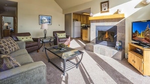 A spacious living room with a fireplace, a television, and a ceiling fan. - Snake River Village 2 Bedroom Apartment by Key to the Rockies (Keystone)