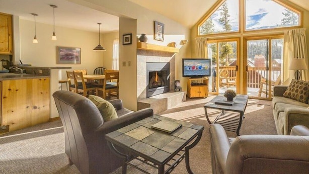 A cozy living room with a fireplace, a television, and a dining area. - Snake River Village 2 Bedroom Apartment by Key to the Rockies (Keystone)