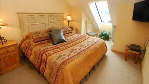 Ein Schlafzimmer mit einem großen Bett, einem Nachttisch, einer Lampe, einem Sessel, einem Fernseher und einem Fenster.