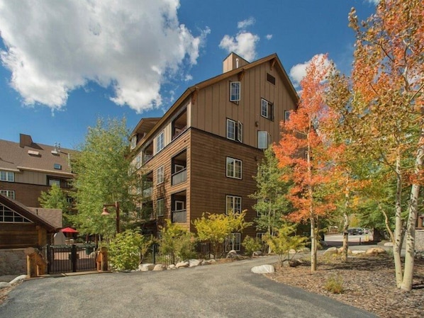 A multi-story building with a wooden facade, a gated entrance, and a driveway leading to a parking area.
