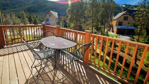 A wooden deck with a table and chairs, surrounded by a wooden railing, overlooking a mountainous landscape.