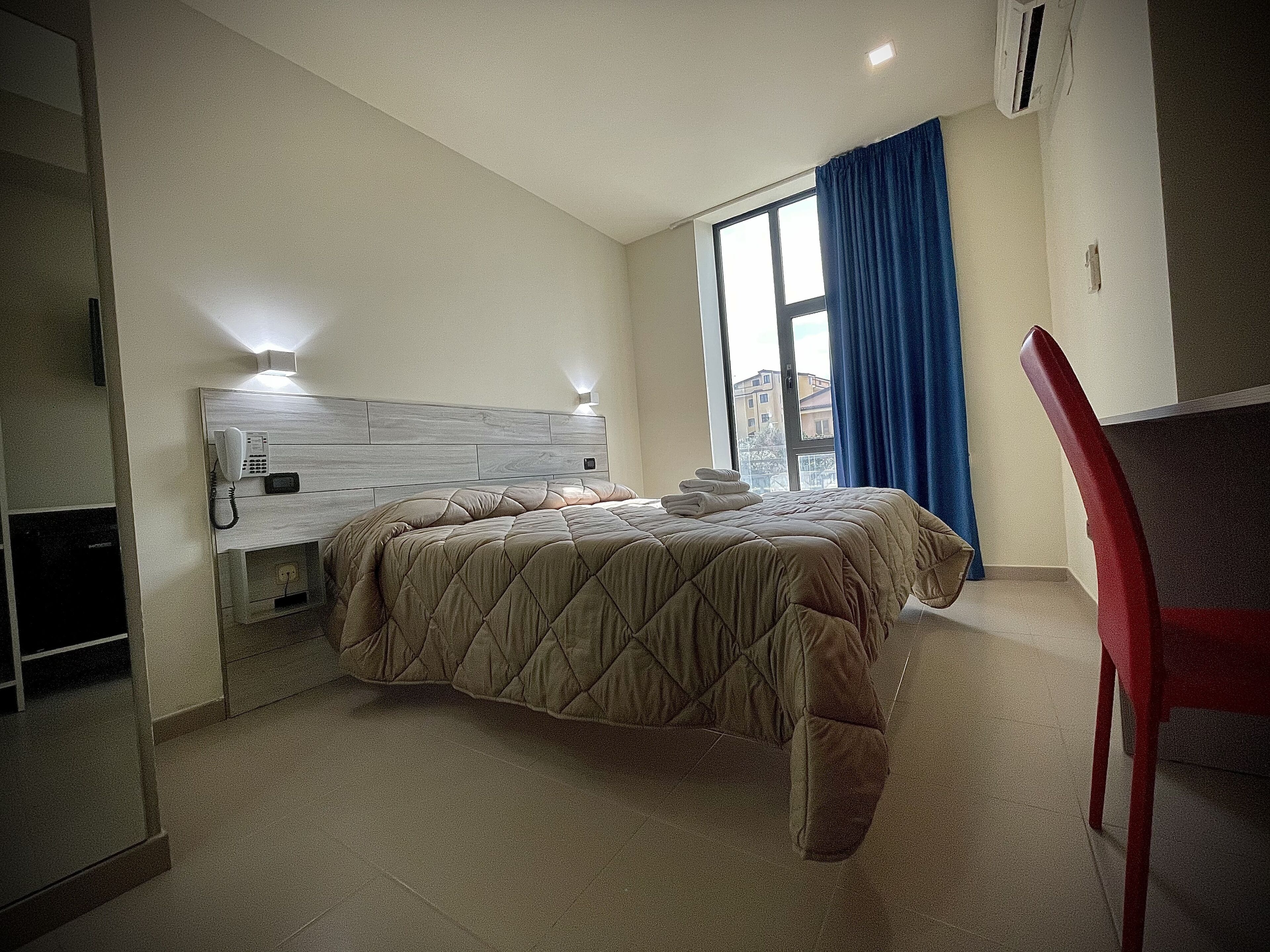 A hotel room with a bed, a desk, a chair, and a window with curtains.