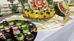 Una mesa con diversos postres, incluyendo una sandía tallada como flor y un plato de pasteles de colores.