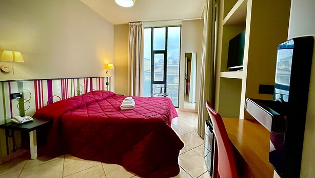 A hotel room with a large bed, a television, a desk with a telephone, and a window with curtains. - Hotel Residence Le Ceramiche (Montalto Uffugo)