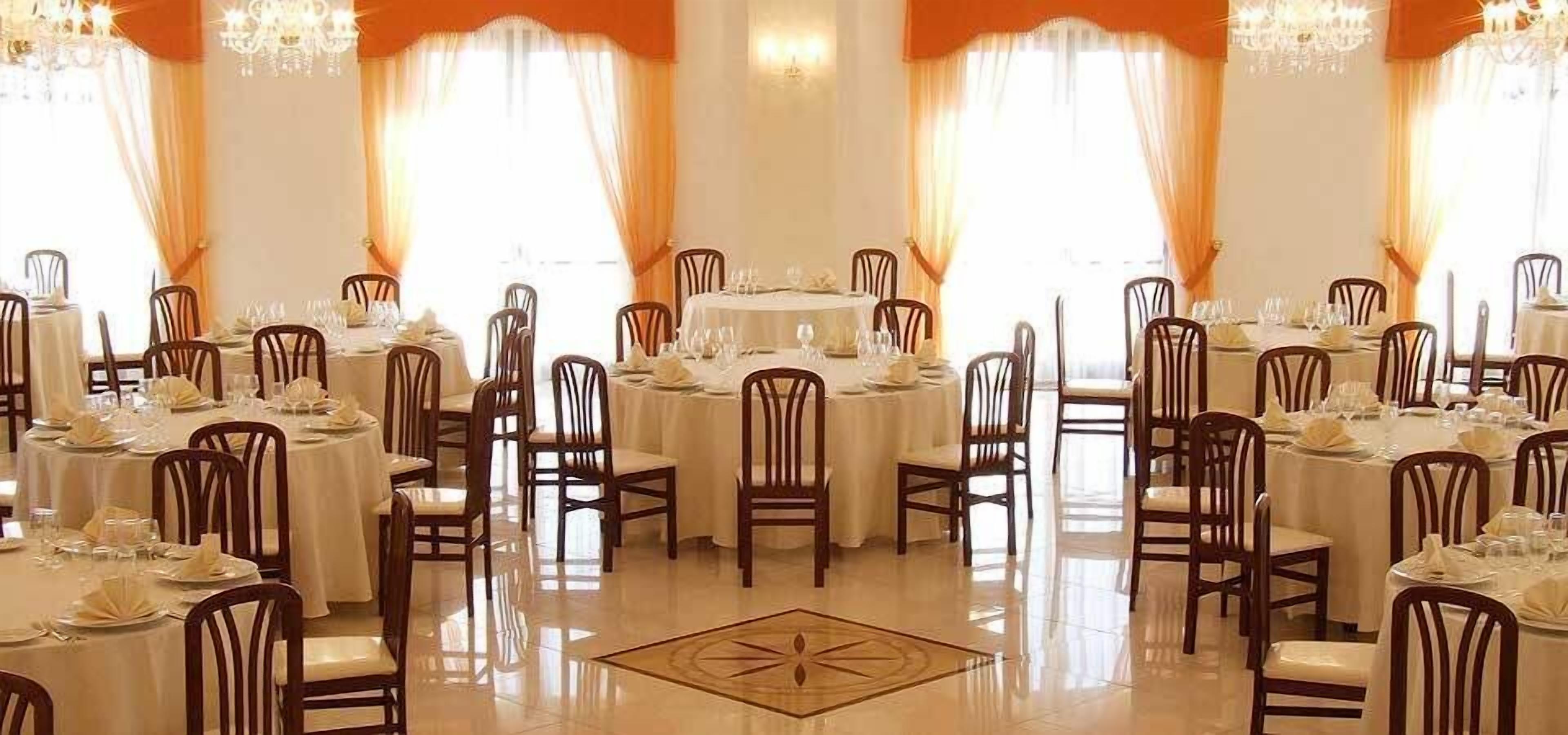 A formal dining room with round tables, chairs, and chandeliers.