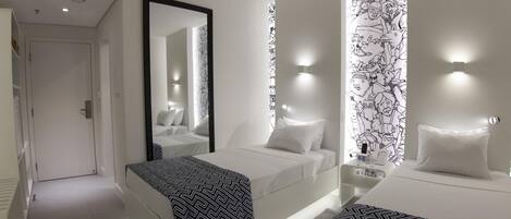 Una habitación de hotel moderna con una cama grande, una cama más pequeña, un espejo y una pared con diseño en blanco y negro.