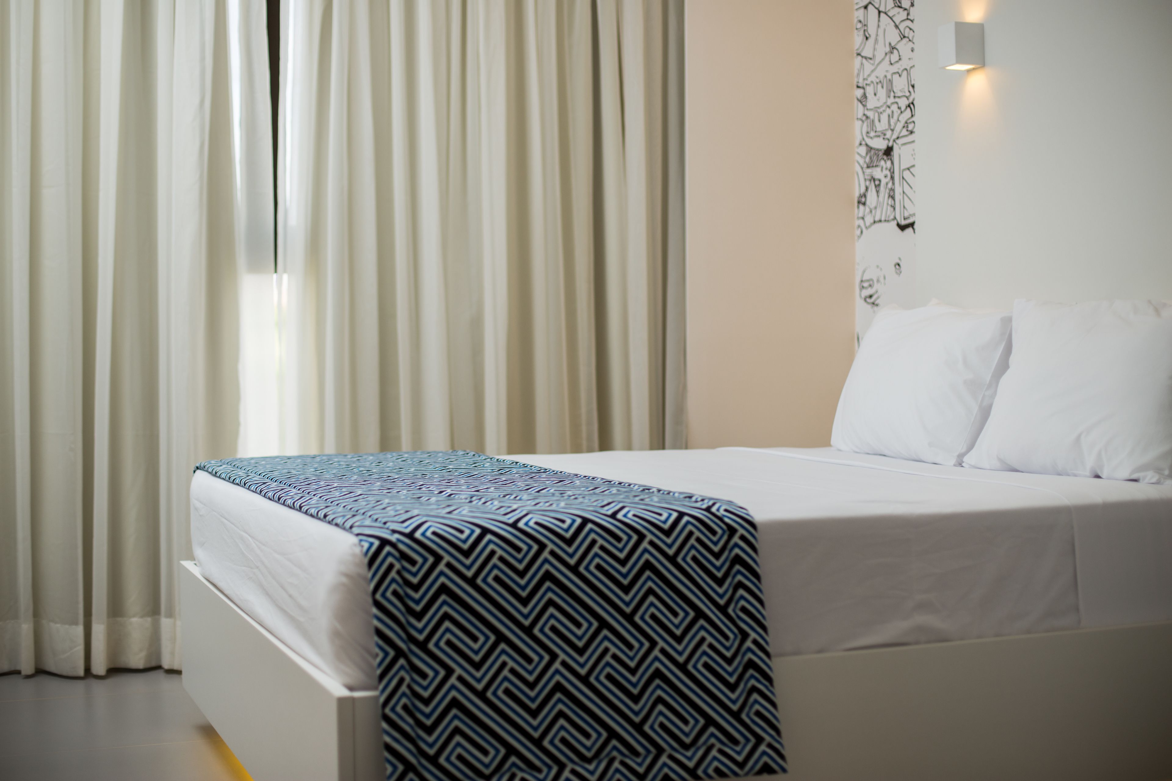 A neatly made bed with a patterned bedspread, white pillows, and a wall-mounted light fixture.