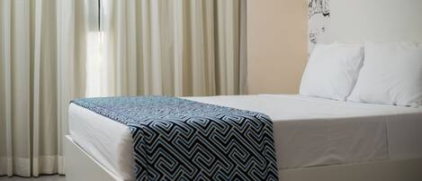 A neatly made bed with a patterned bedspread, white pillows, and a wall-mounted light fixture.