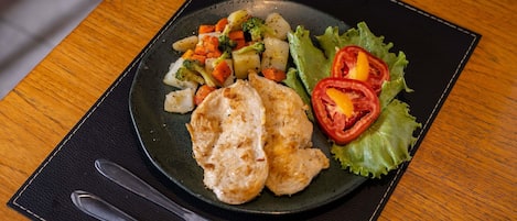 A plate of food with vegetables and a piece of chicken on a black plate, placed on a black placemat.