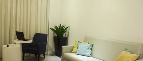 A modern living room with a sofa, a chair, a small table with a laptop, a potted plant, and a round side table.