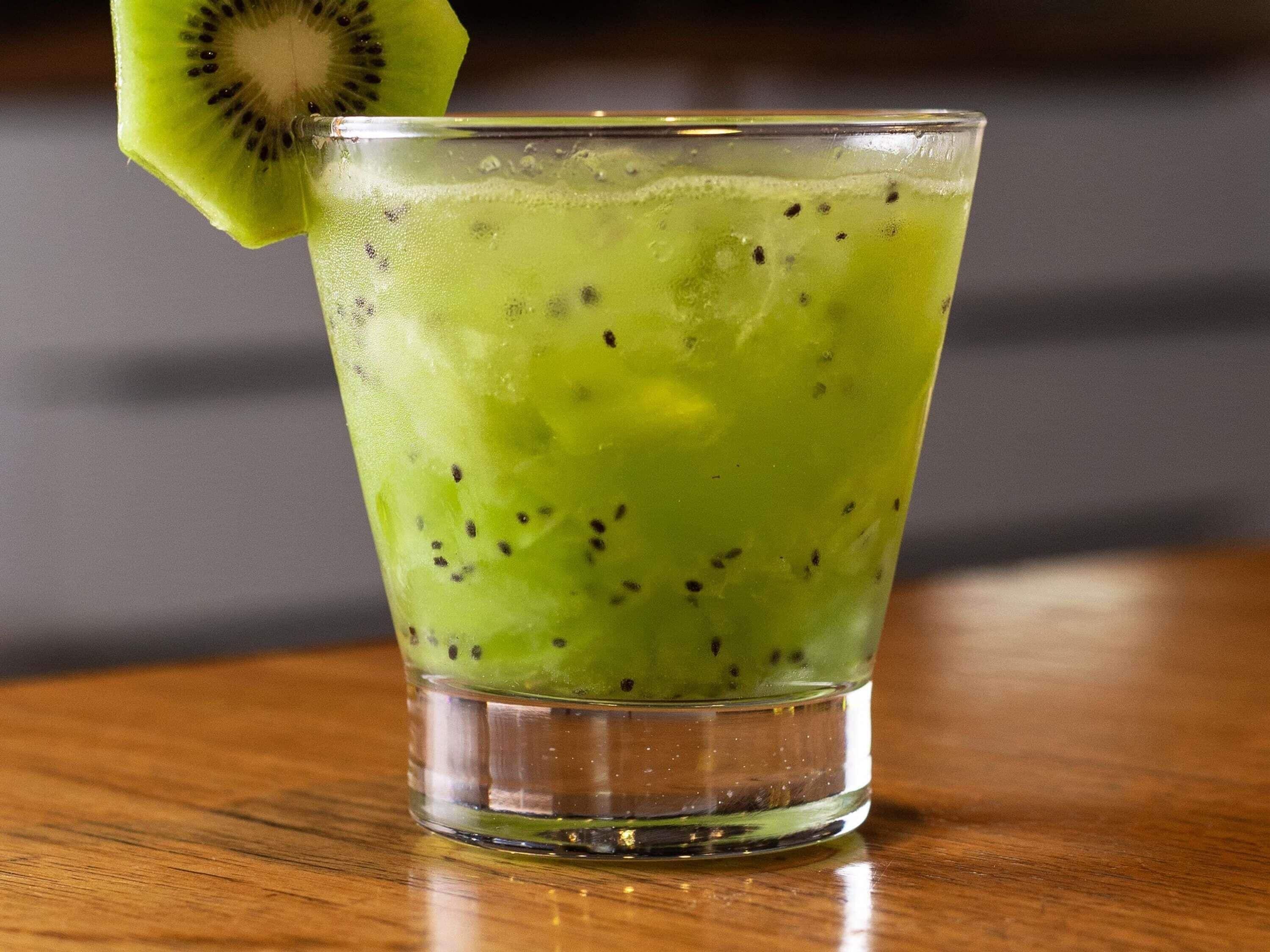 Un vaso de bebida verde con una rodaja de kiwi en el borde, sobre una superficie de madera.