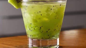 Un vaso de bebida verde con una rodaja de kiwi en el borde, sobre una superficie de madera.
