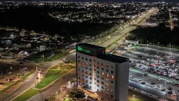Un hotel de varios pisos con un letrero en la azotea, rodeado por un estacionamiento y una calle.