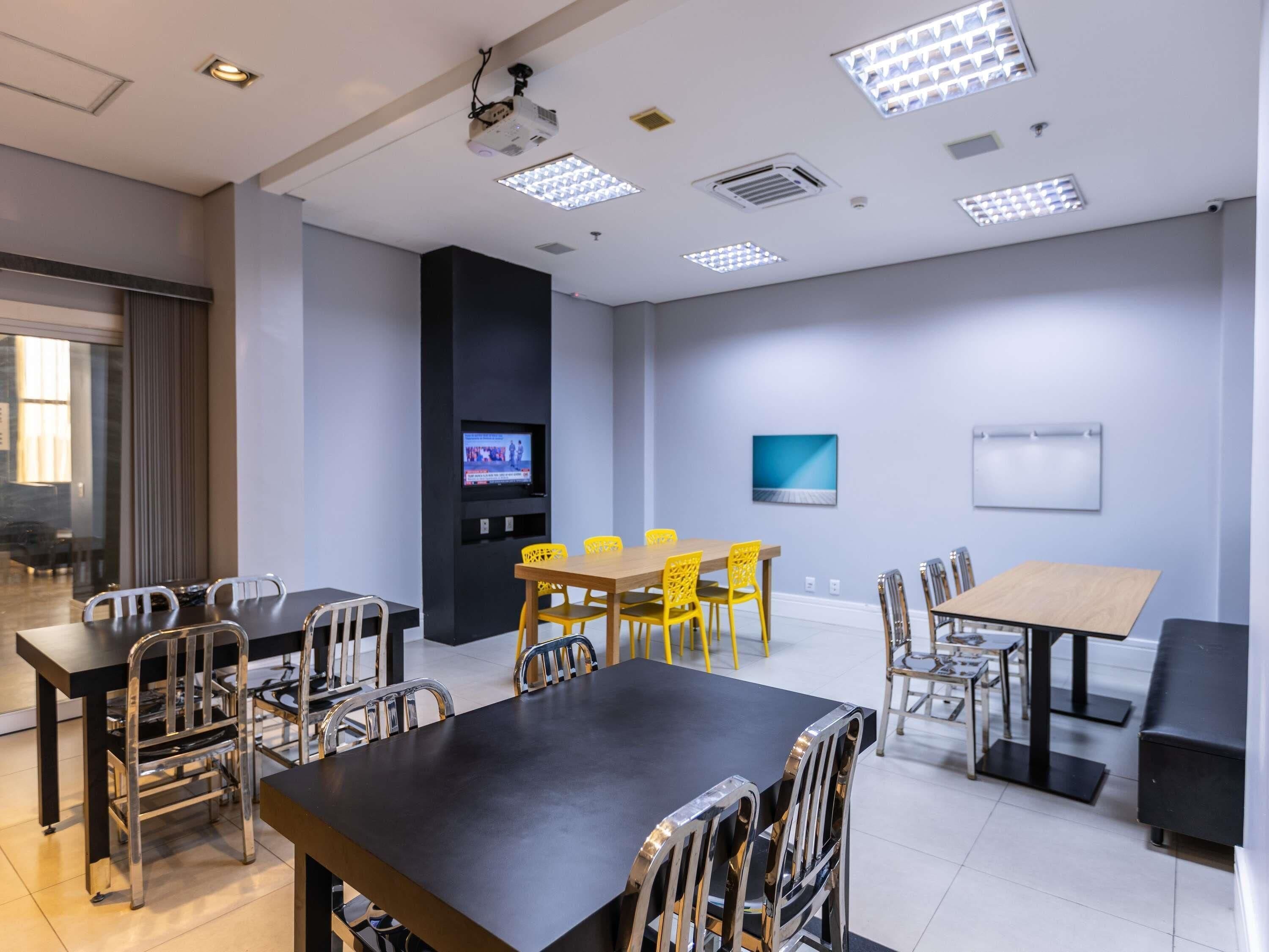 Una sala de conferencias con una gran mesa, sillas, un proyector, un televisor y una pizarra.