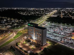 Un hotel de varios pisos con letrero en la azotea, estacionamiento y área urbana circundante.