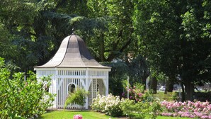 A gazebo with a conical roof surrounded by lush gardens and flowering plants. - Hotel Rosengarten  (Zweibruecken)