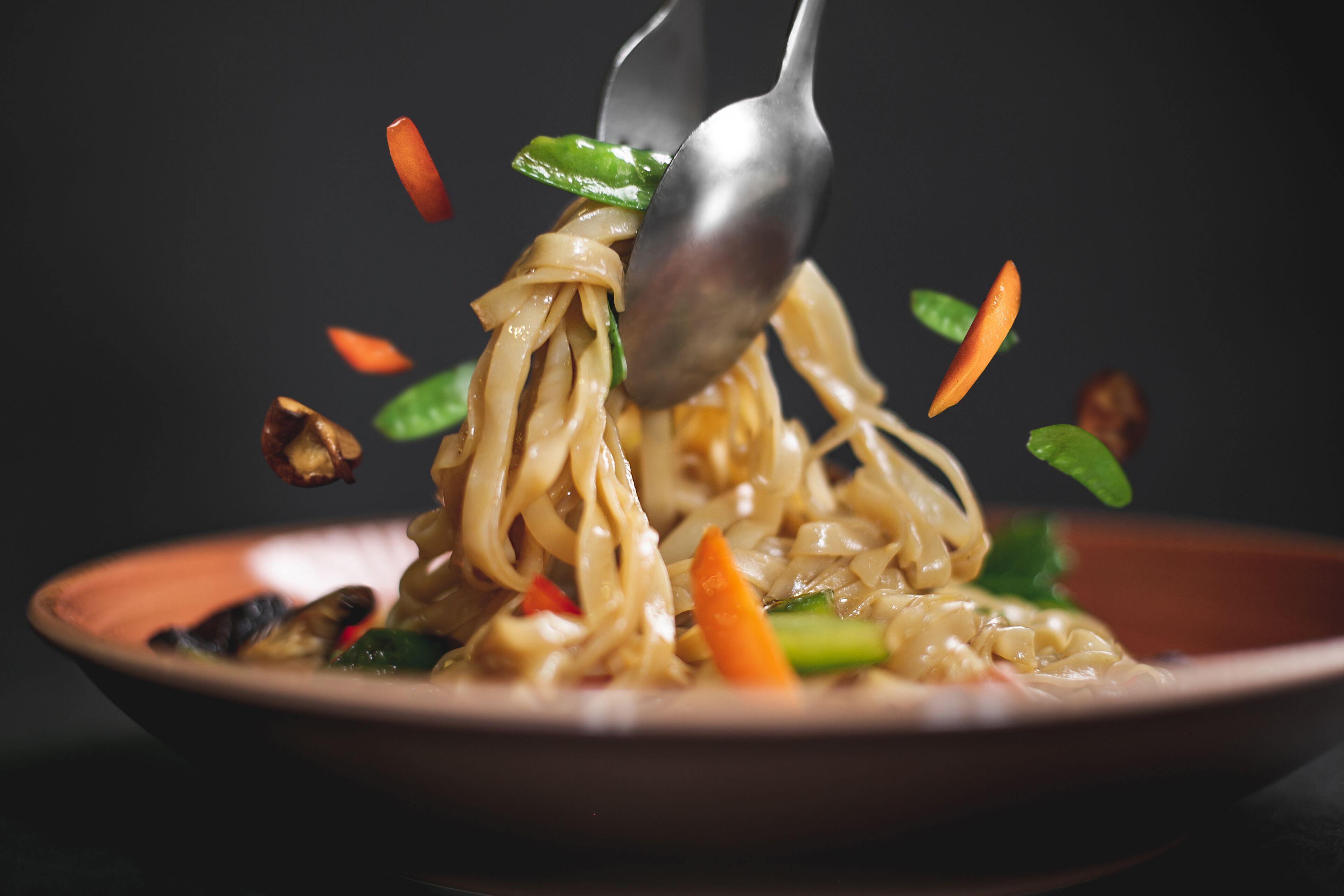Un tazón de fideos con verduras y una cuchara levantando algunos fideos.