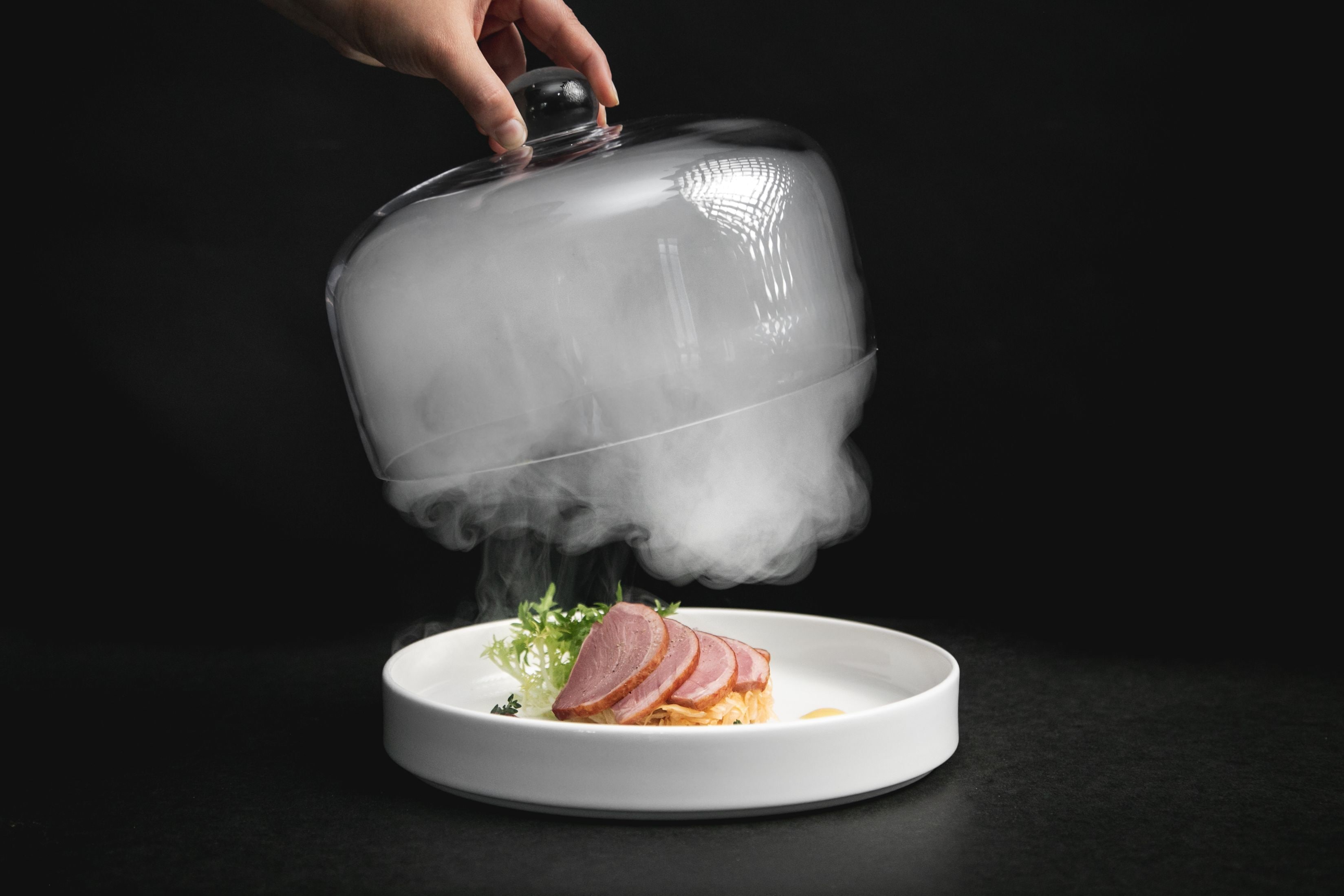 A white plate with sliced ham and a garnish on a black surface.