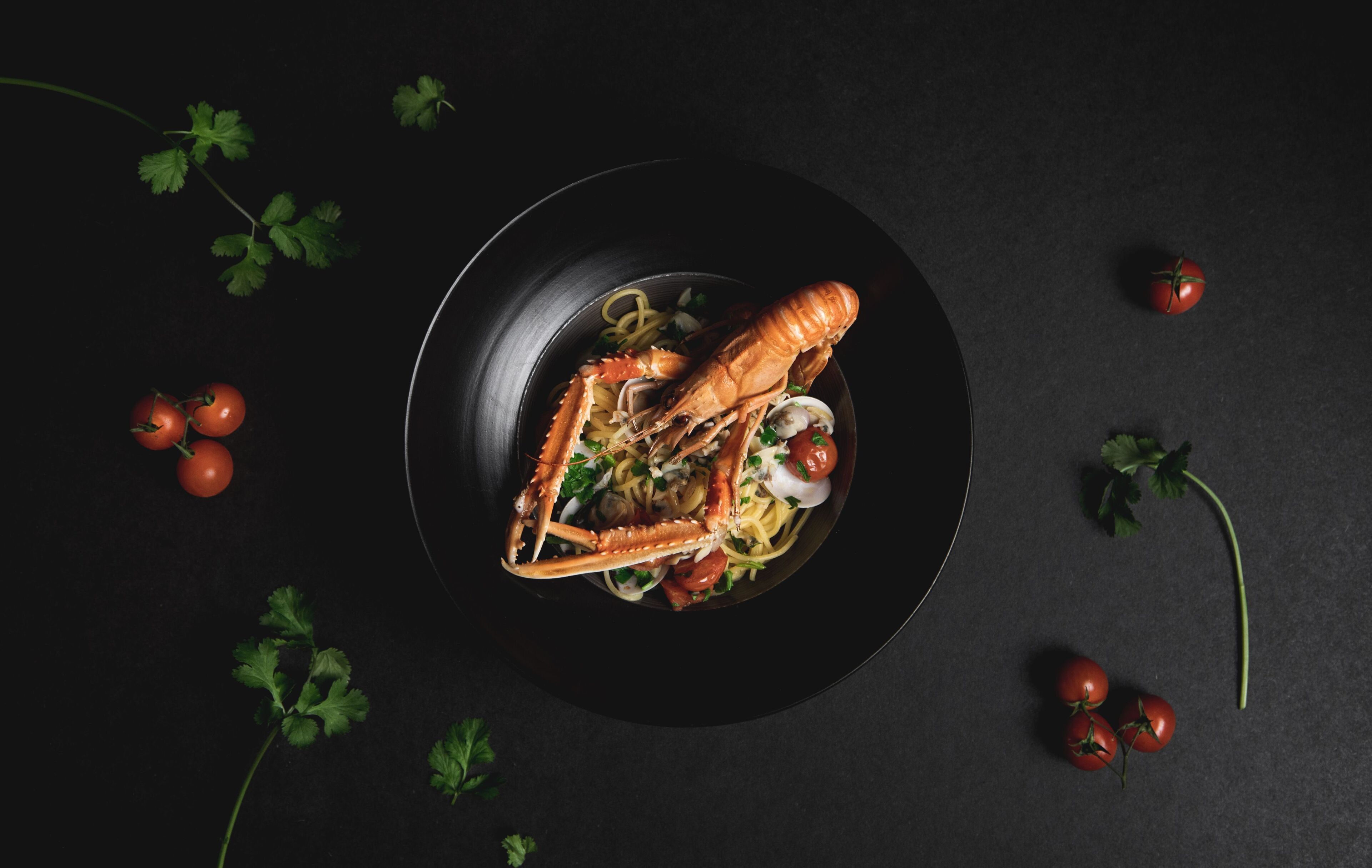 Un plato de langosta sobre una superficie oscura, con tomates y perejil.
