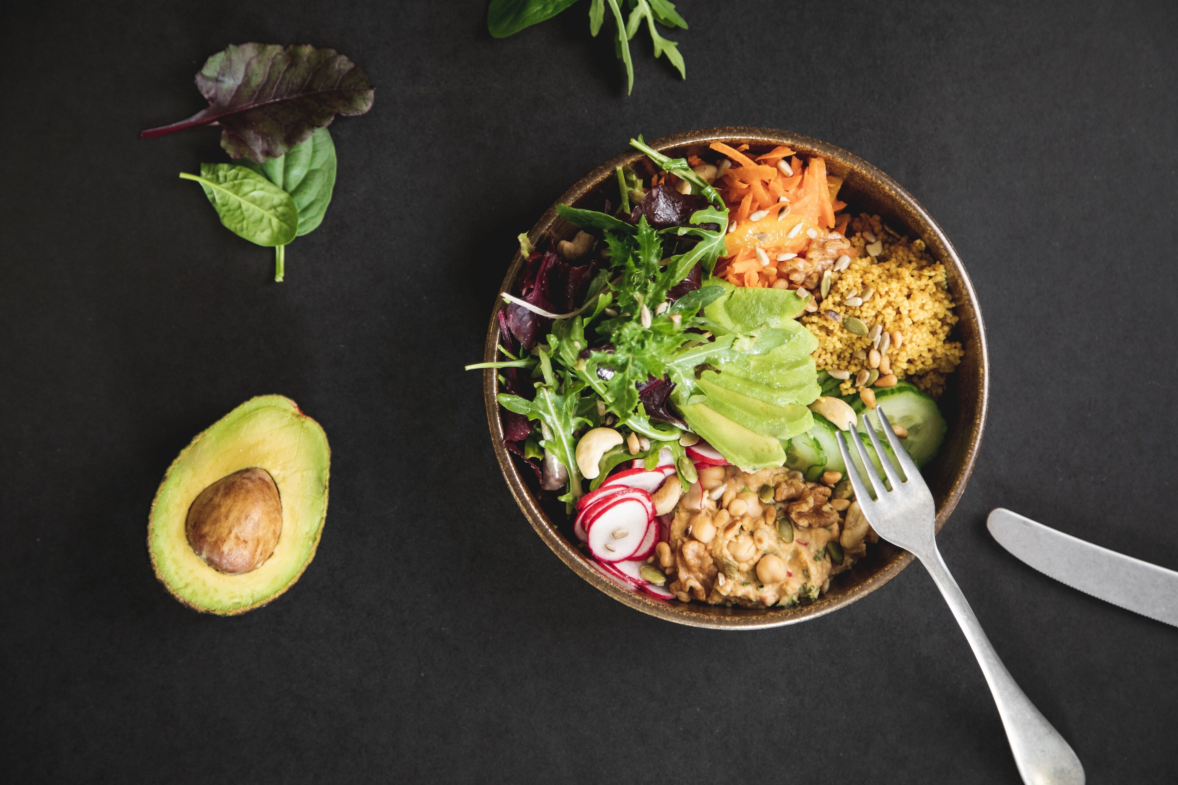 Un tazón de ensalada con diversos vegetales y nueces, sobre una superficie oscura.