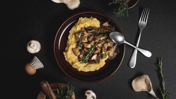 A plate of mashed potatoes topped with mushrooms and herbs, accompanied by a fork and spoon on a dark surface.