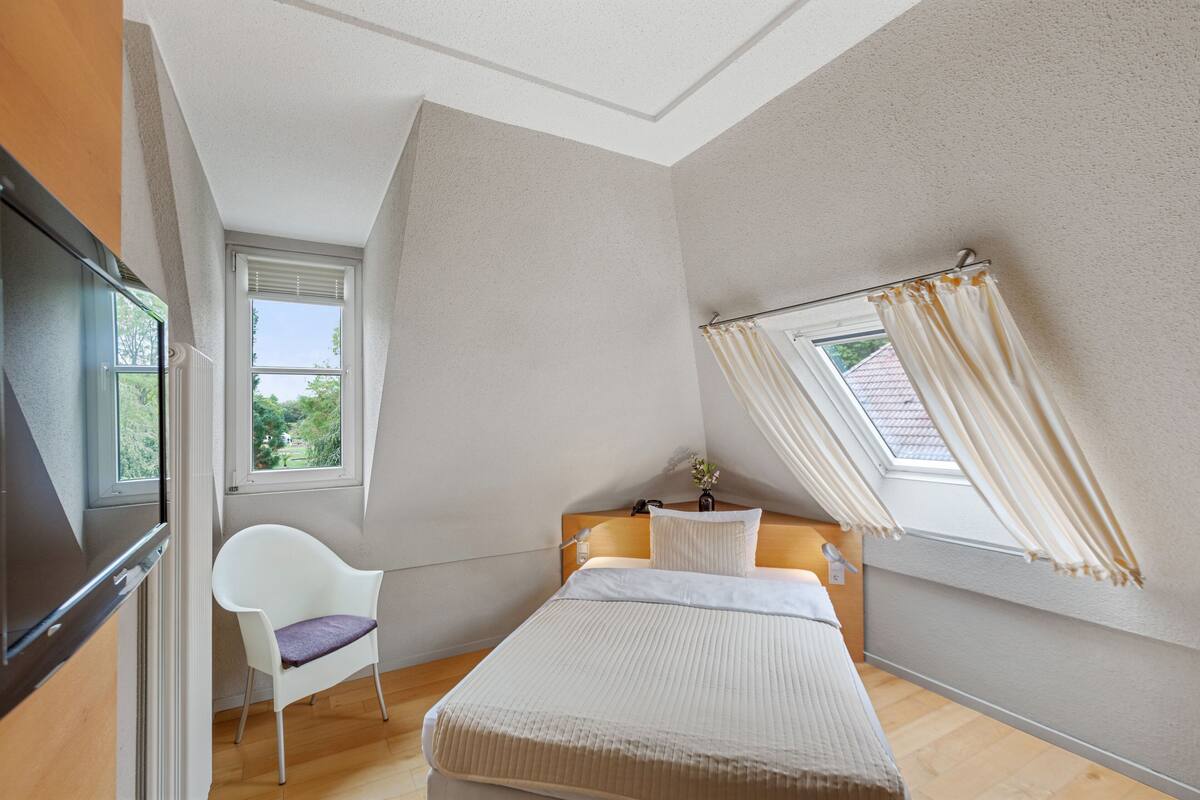 Ein Schlafzimmer mit Bett, einem Sessel, einem Fenster und einem Oberlicht.