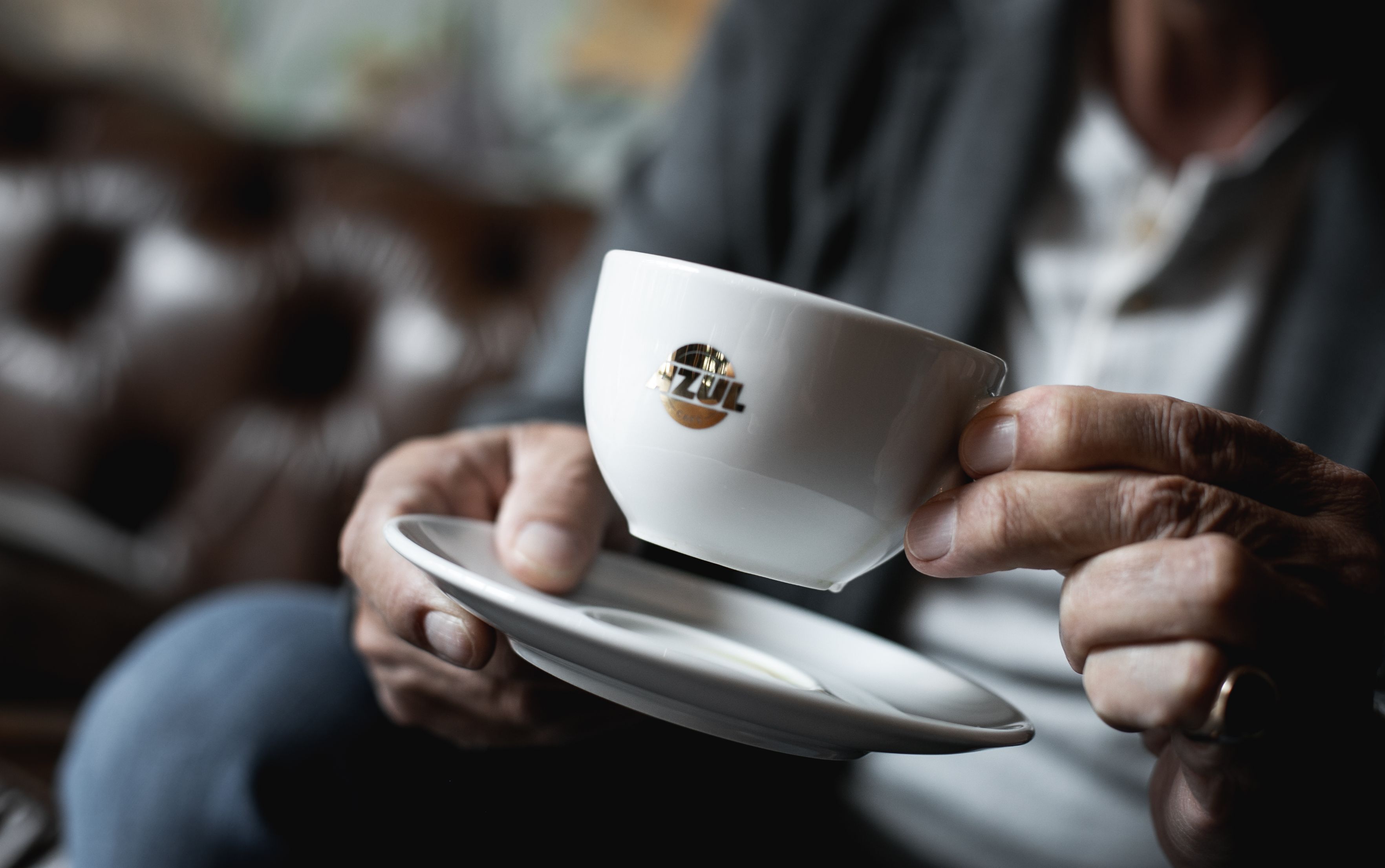 A person holding a white cup with a logo, seated with a blurred background.