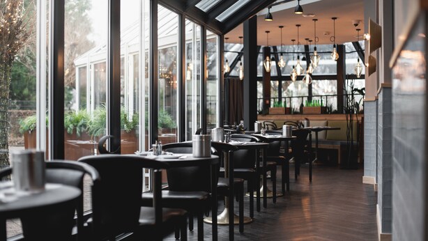 A restaurant with large windows, tables, chairs, and hanging light fixtures. - Hotel Rosengarten  (Zweibruecken)