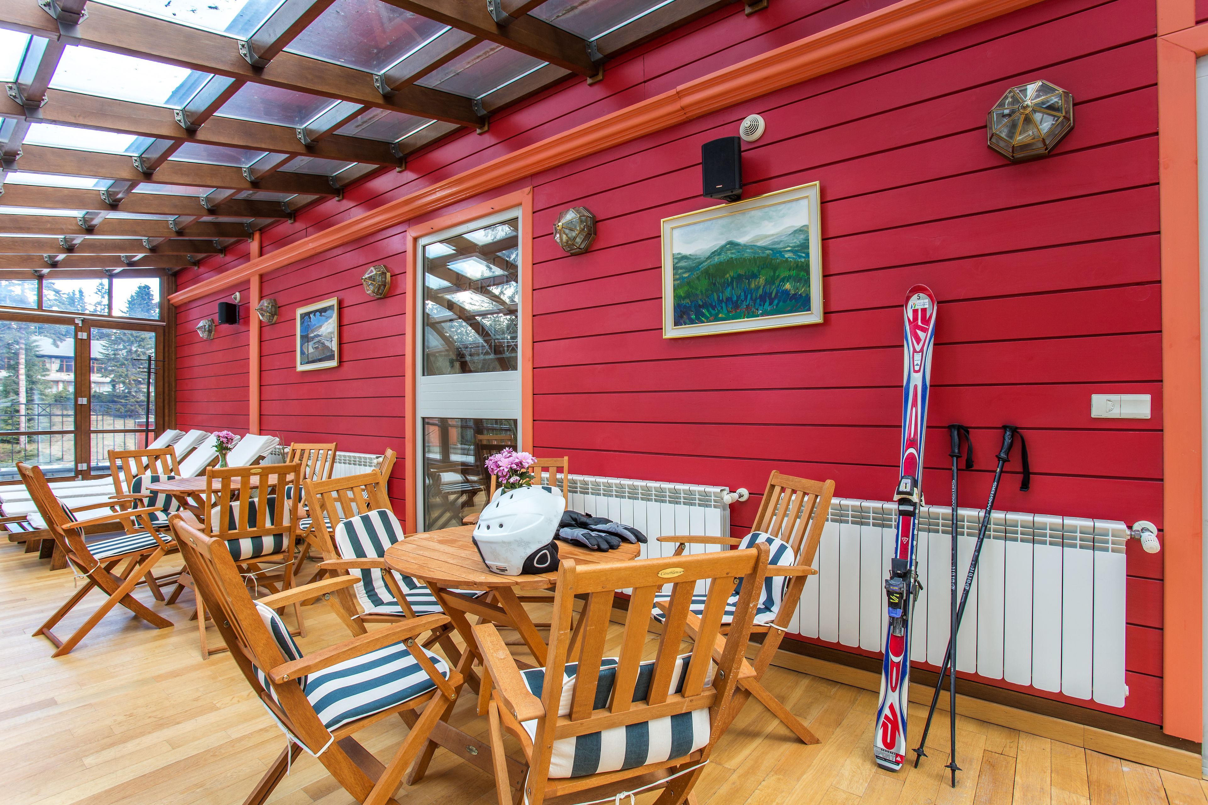 Una habitación con sillas y mesas de madera, un esquí y una pared roja con un cuadro.