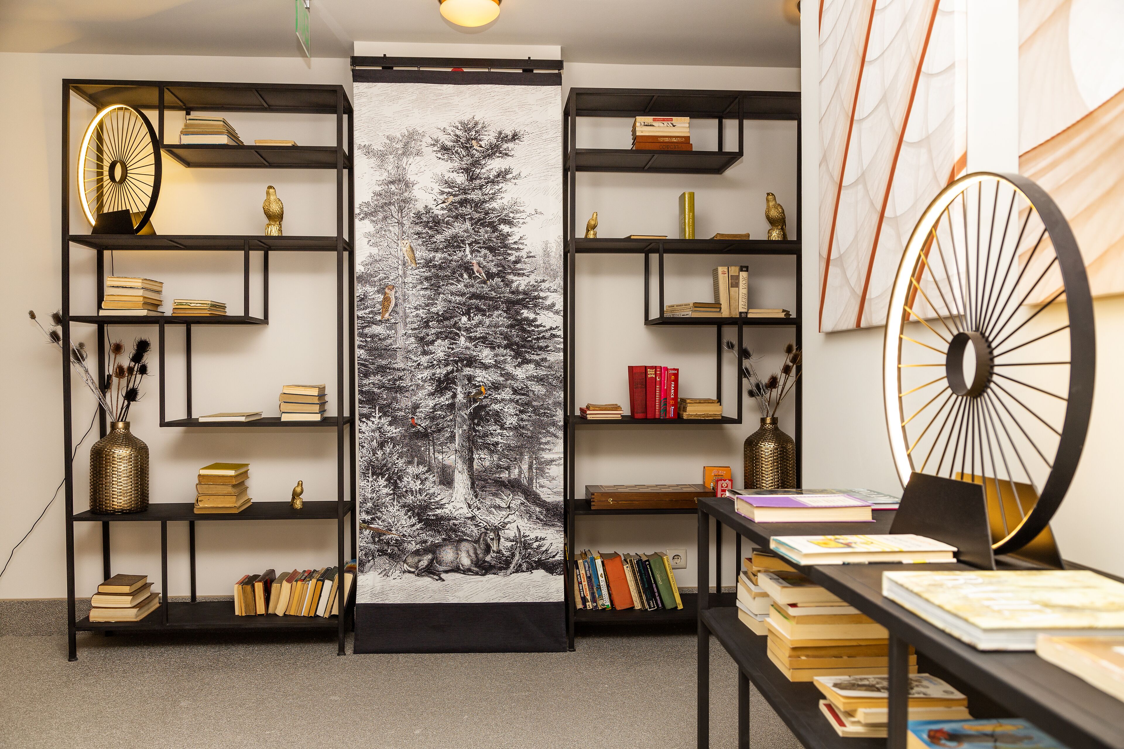 Una habitación con estanterías, un cuadro grande de un bosque y una rueda decorativa.