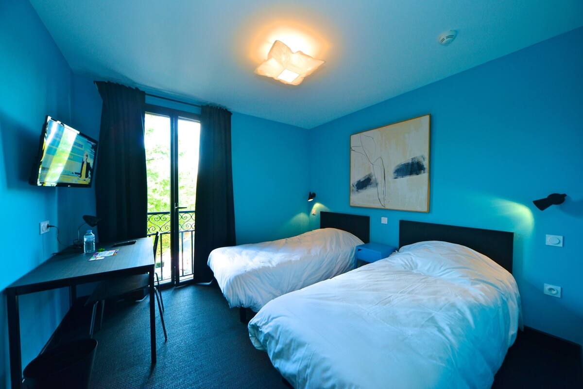 A hotel room with two beds, a desk, a television, and a window with curtains.