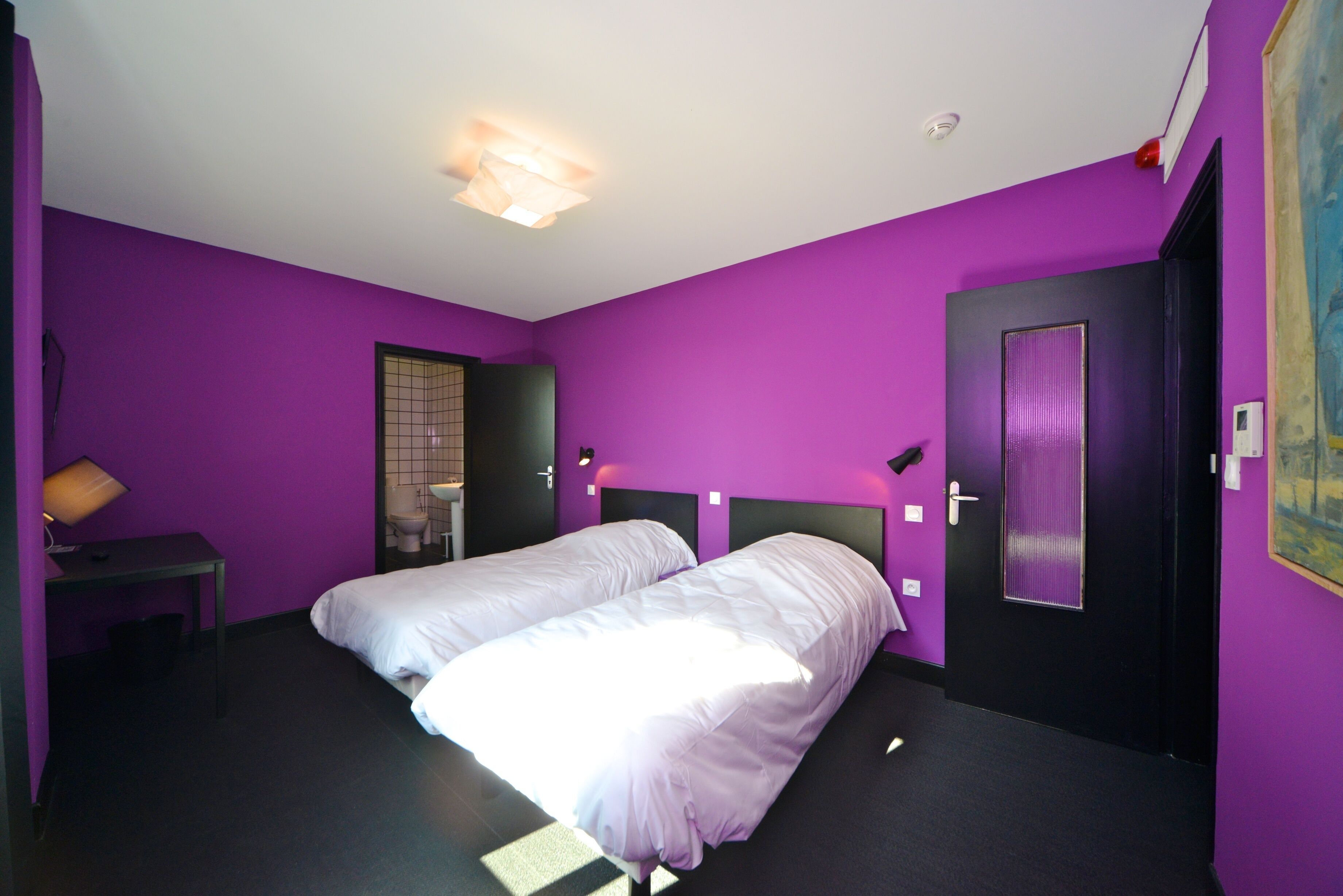 A room with two beds, a desk, a mirror, and a door.