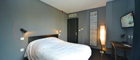 Una habitación de hotel con cama, escritorio, silla, televisor y puerta.