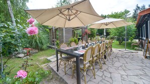 An outdoor patio with a table and chairs, surrounded by greenery and a stone floor.
