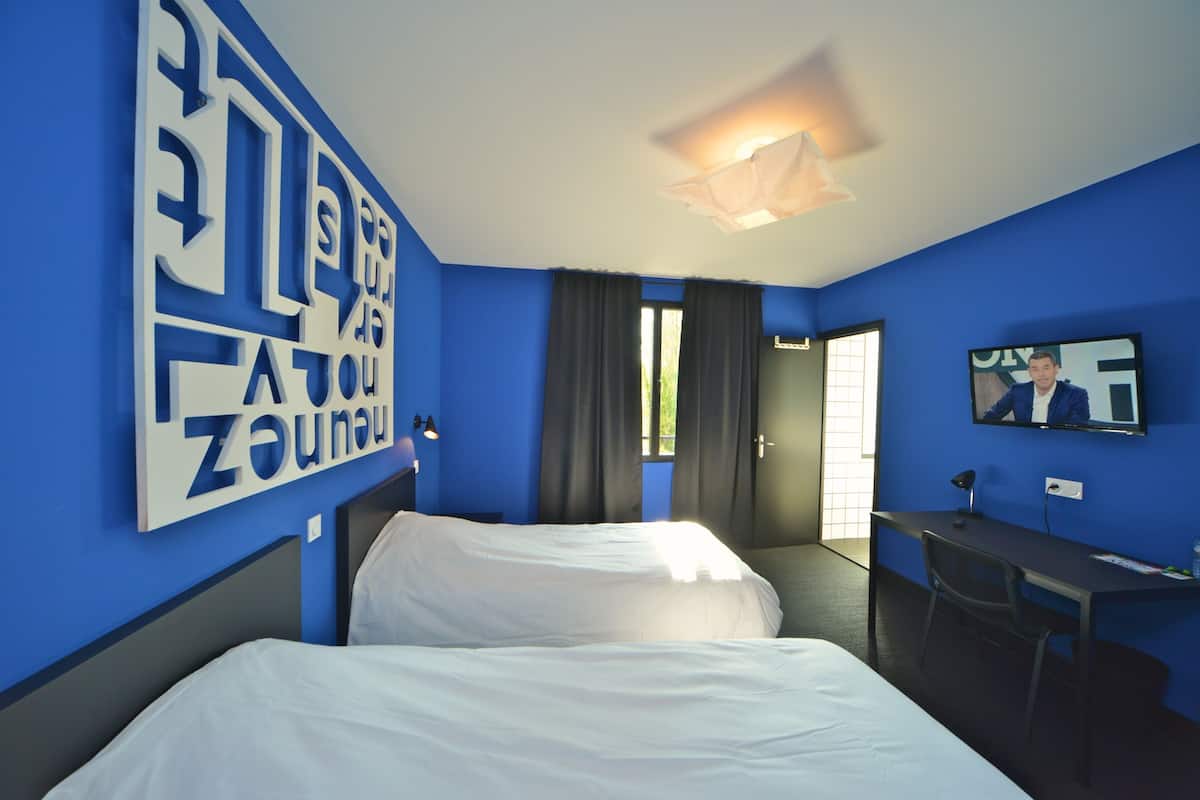 A hotel room with a bed, a desk, a chair, a television, and a large window with curtains.