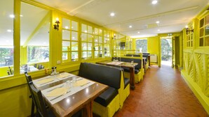 A restaurant with yellow walls, wooden tables, and black cushioned booths.