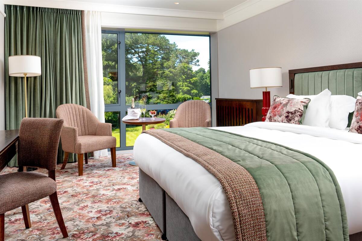 Une chambre d’hôtel avec un grand lit, deux fauteuils, un bureau et une vue sur l’extérieur.