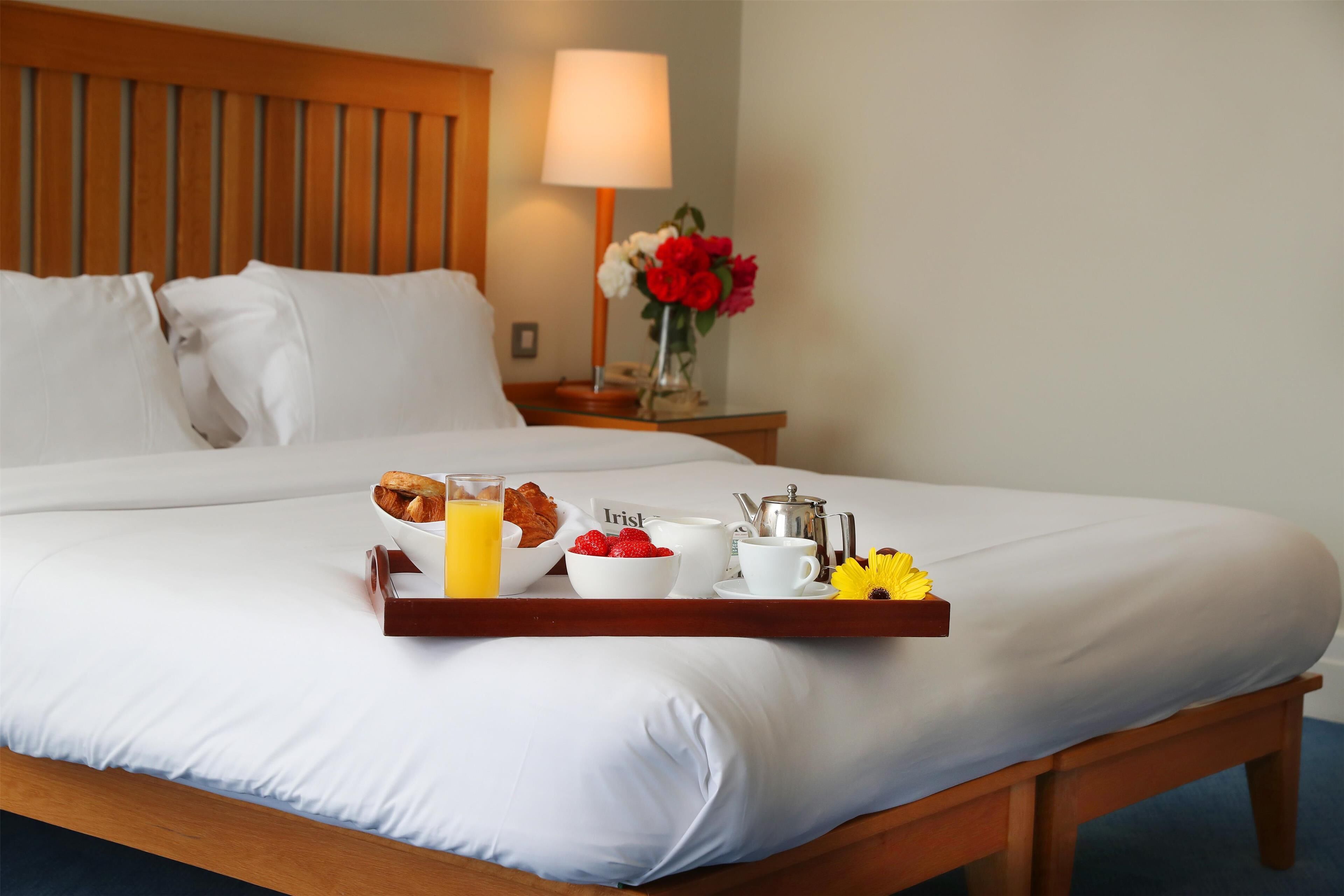 A neatly made bed with a tray of breakfast items including croissants, strawberries, and orange juice.