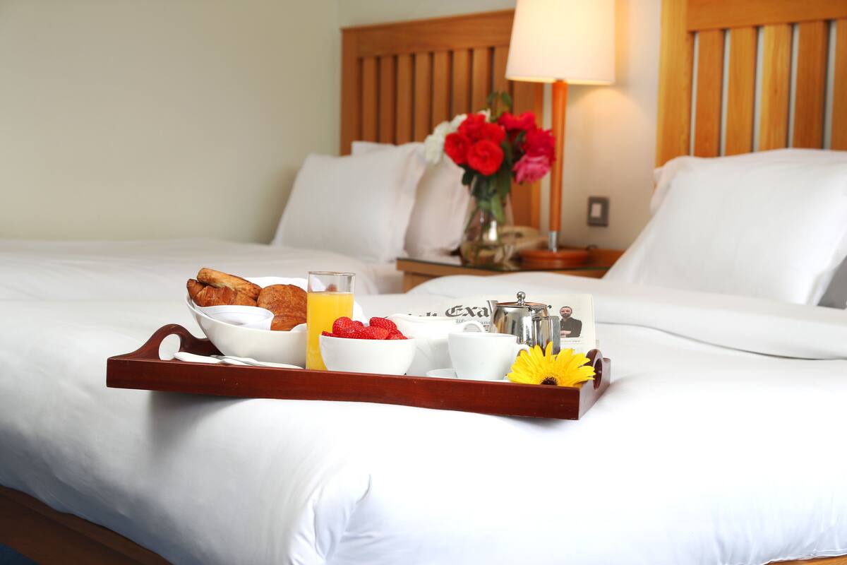 Un lit bien fait, avec un plateau contenant divers éléments pour le petit-déjeuner, notamment des croissants, des fraises et du jus d’orange.