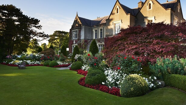 A large, historic building with a well-manicured garden, featuring neatly trimmed hedges and a variety of flowering plants.